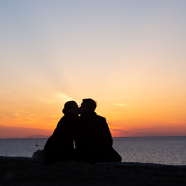 Couple sitting in front of the sunset at the sea. The colours of the sunset in Greece are insanely beautiful.