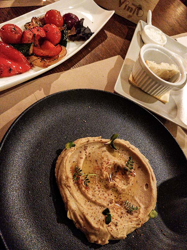 In the front, hummus on a plate. In the back grilled veggies.