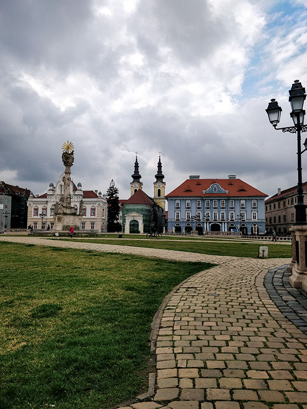 A square with grass and walkways, in the back old, colourful buildings.