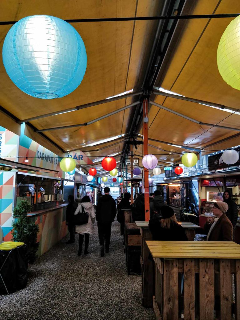 Street food area with many stalls on the left and right side, in the middle standing tables.
