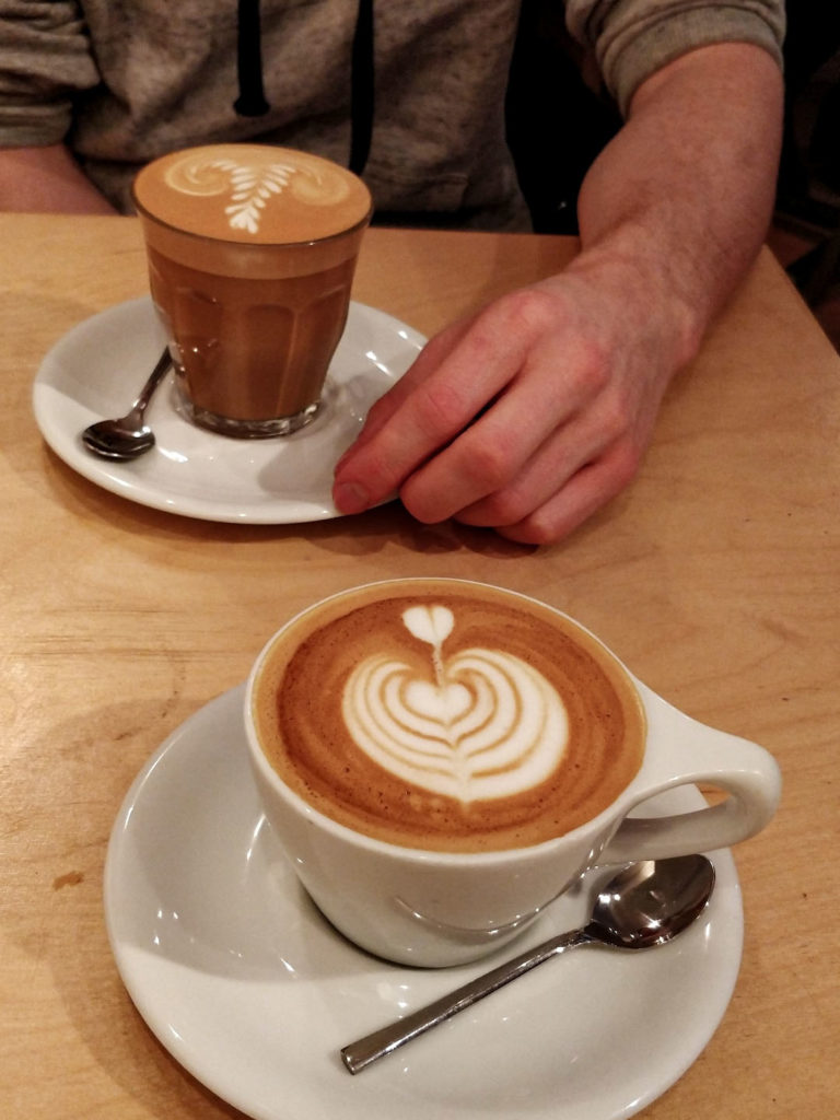 Two coffees on a wooden table. The coffees have beautiful latte art in the form of tulips.