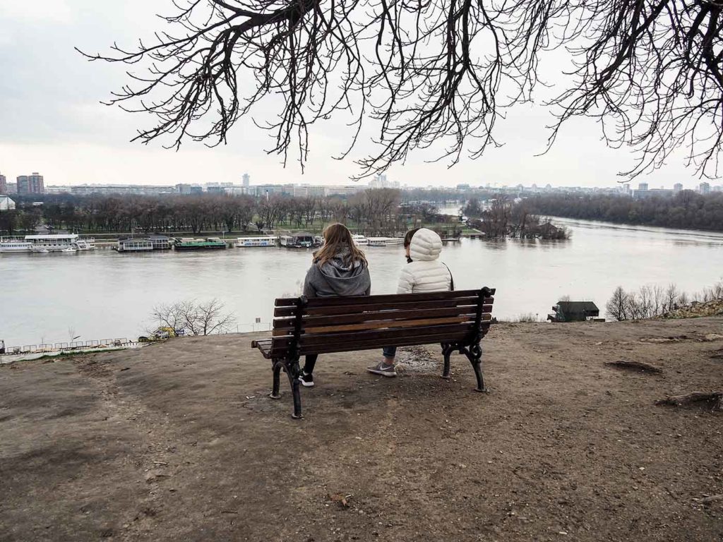 Two girls sitting on a bench overlooking a river and the city of Belgrade.