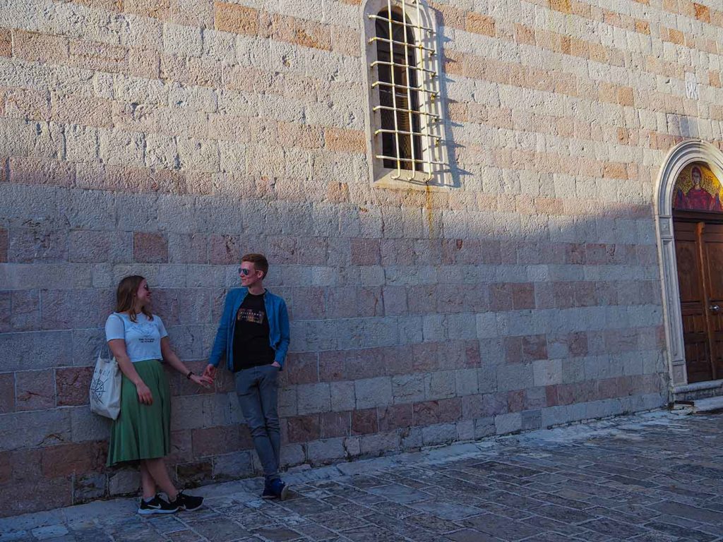 On the left side two people holding hands and leaning against a wall. The wall is tall and covers the whole picture. On the right side a door in the wall.