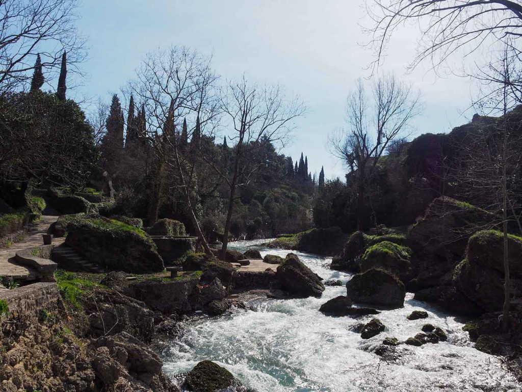 A landscape picture of a small river making its way around rocks. On the left side a path leading up a small hill.