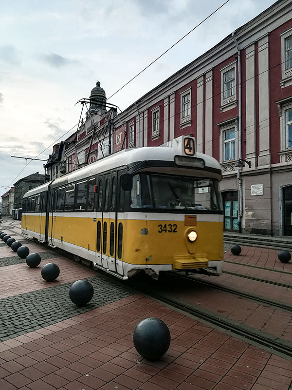 In the middle a yellow tram in front of a red-pinkish old building.